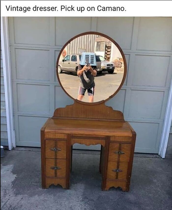 Vintage dresser with a round mirror reflecting a person holding an air conditioner unit on their head on Facebook Marketplace post.