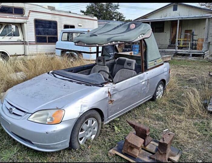 Silver convertible car with a crocodile head roof attachment parked in a yard among old vehicles, unhinged Facebook Marketplace listing.
