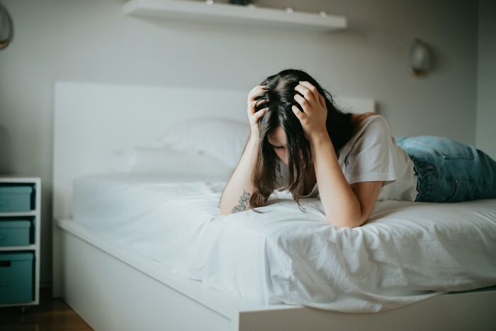 Young woman stressed on a bed, holding her head, illustrating regret and frustration from life hacks gone wrong.