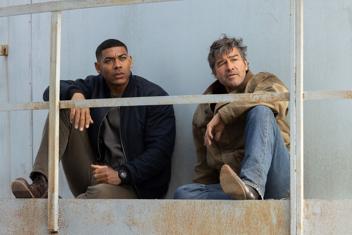 Two men sit on a metal platform, with a focus on Lanterns teaser revealing Hal Jordan&rsquo;s suit details.