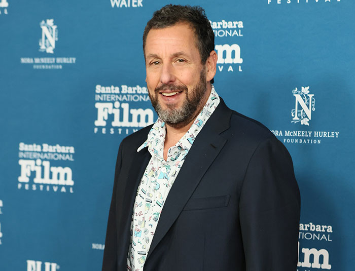 Adam Sandler at Santa Barbara International Film Festival, dressed in patterned shirt and dark blazer, smiling for cameras.