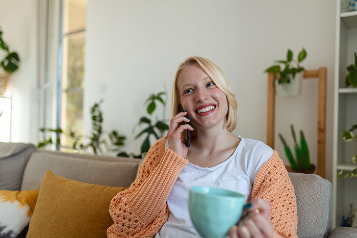 Smiling woman holding a teal mug and talking on the phone, illustrating real-life cheat codes shared by people.