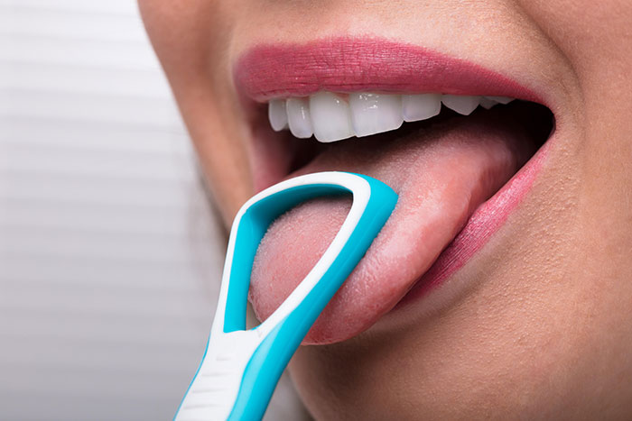 Close-up of a person using a tongue scraper as a real-life cheat code for better oral hygiene and fresh breath.