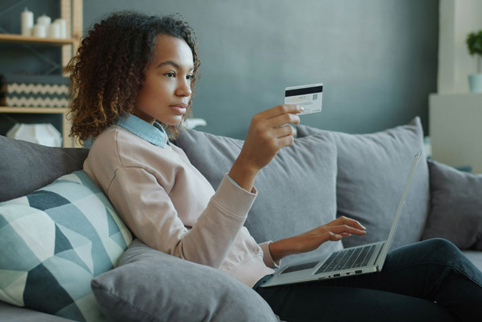 Woman using laptop and credit card on couch, illustrating real-life cheat codes for online shopping and savings.