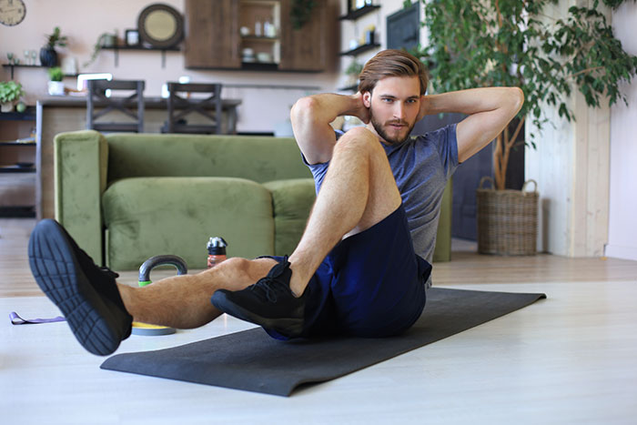 Man performing an ab workout on a mat at home, demonstrating real-life cheat codes for effective fitness results.
