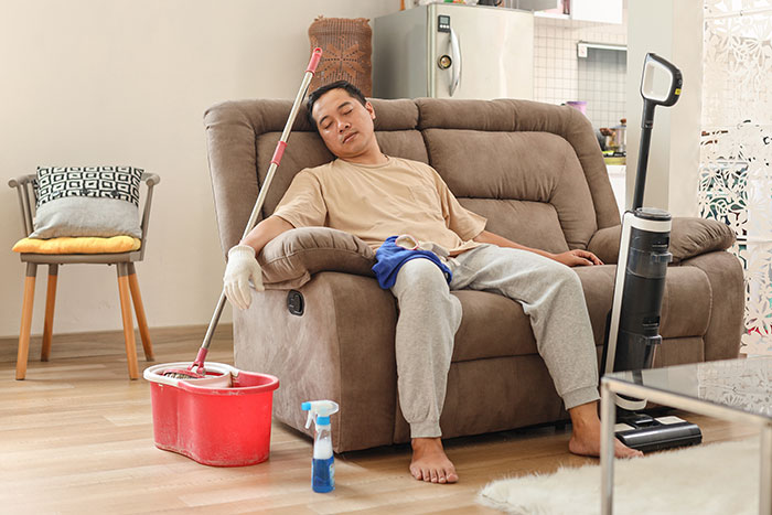 Person resting on a sofa surrounded by cleaning tools, illustrating real-life cheat codes for easier household chores.