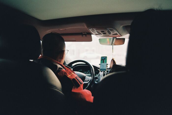 Man driving a car, viewed from the backseat, showing a dad supporting his kids in a wholesome moment.
