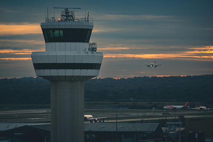 Torre de controle de tráfego aéreo ao pôr do sol com um avião se aproximando da pista, relacionado à análise de acidentes da Aviation Experts e da Air Canada. Torre de controle de tráfego aéreo ao pôr do sol com um avião se aproximando da pista, relacionado à análise de acidentes da Aviation Experts e da Air Canada.
