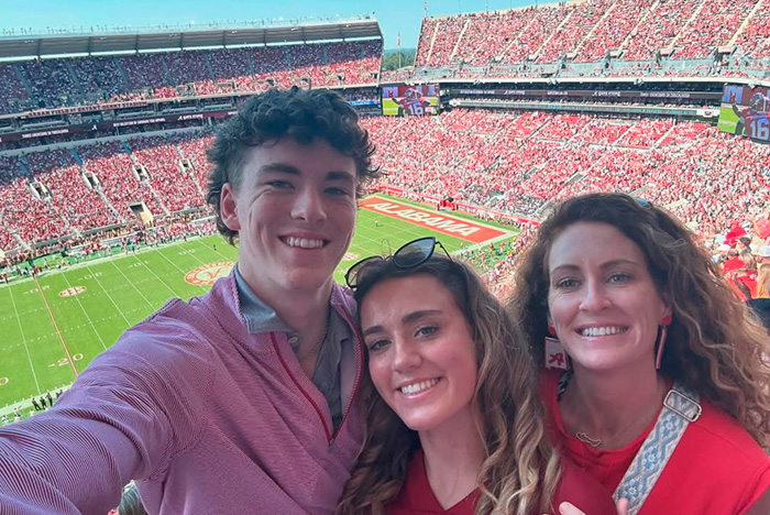Três pessoas sorridentes em um estádio de futebol lotado do Alabama, relacionadas à causa dolorosa da morte de um estudante do Alabama. Três pessoas sorridentes em um estádio de futebol lotado do Alabama, relacionadas à causa dolorosa da morte de um estudante do Alabama.