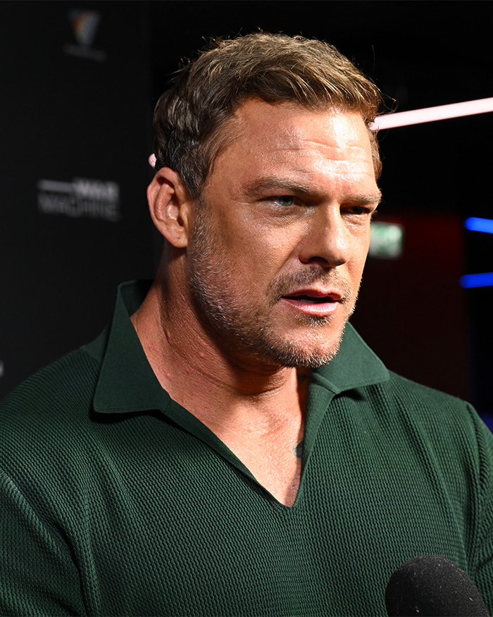 Alan Ritchson speaking at an event, wearing a dark green shirt, with close-up bodycam footage details highlighted.