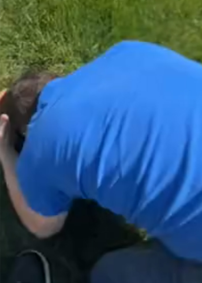 Man in blue shirt crouching on grass during Alan Ritchson’s bodycam footage of brutal neighbor confrontation starting.