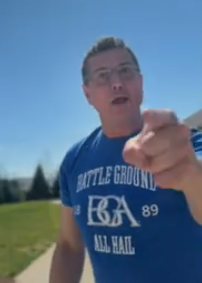 Man in blue shirt pointing aggressively outdoors, captured in Alan Ritchson bodycam footage of brutal neighbor confrontation.
