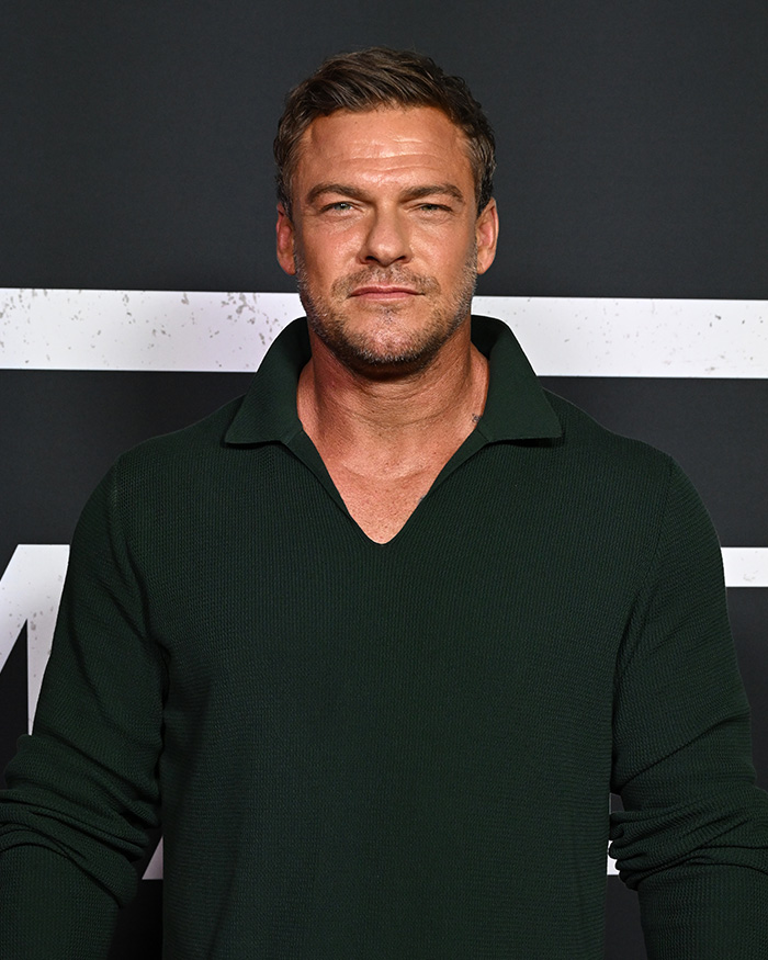 Alan Ritchson wearing a dark green sweater, posing at an event, speaking out about wild fight with neighbor.