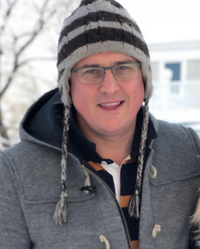 Man wearing glasses and a winter hat, outdoors in the snow, related to Alan Ritchson wild fight with neighbor topic.