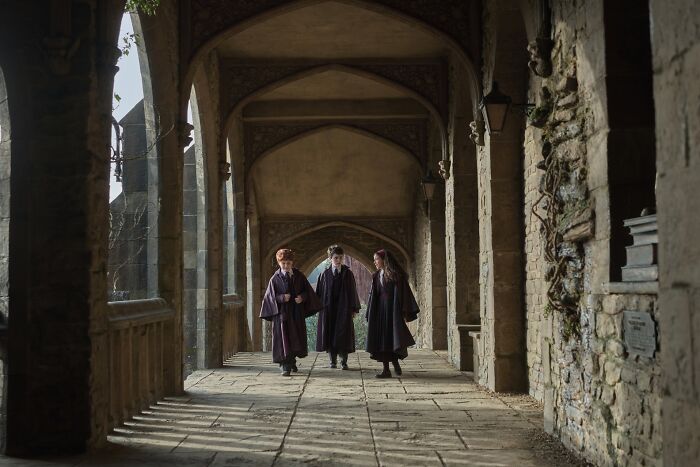 Three young characters in wizard robes walk through a stone corridor in the Harry Potter series trailer scene. Three young characters in wizard robes walk through a stone corridor in the Harry Potter series trailer scene.