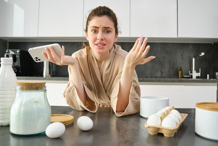 Young woman in bathrobe looking confused in kitchen with eggs and milk on the counter, representing picky eater allergy excuse.