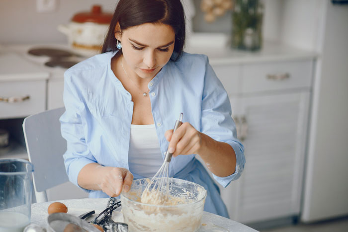 Young woman whisking batter in kitchen, representing picky eater secretly enjoying regular food despite claimed allergy.