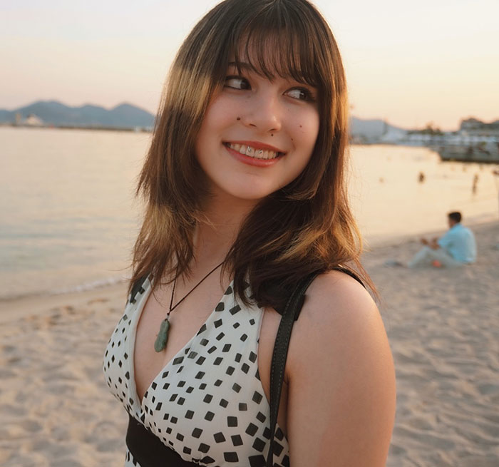Young woman smiling at sunset on the beach, representing Olympic hero Alysa Liu in a casual summer dress.
