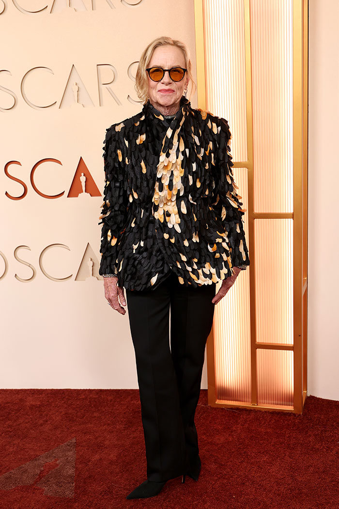 Person wearing an avant-garde textured jacket and sunglasses posing on the red carpet at the Oscars 2026 Hollyweirdos event.