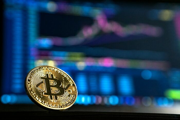 Gold Bitcoin coin resting in front of a blurred stock market chart representing shaky industries vulnerable to collapse.