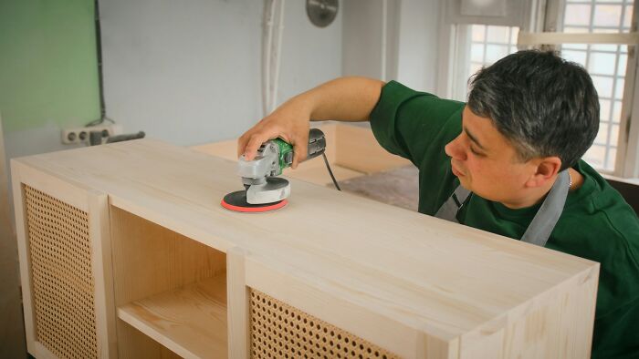 Person using a power sander on wooden furniture, demonstrating a premium-tier life hack for woodworking projects.