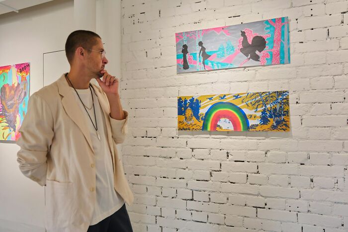 Man in a beige jacket observing colorful bizarre art on a white brick wall, reflecting on true stories that sound unbelievable.