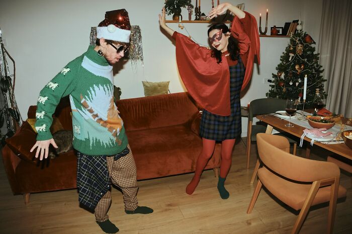 Two people wearing quirky outfits dancing indoors with Christmas decorations, showcasing weird family traditions.