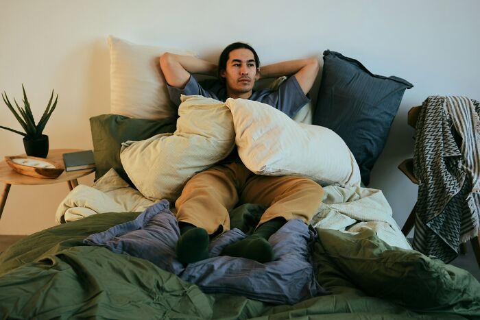 Person resting on a bed surrounded by pillows and blankets, embodying a premium-tier zombie life hack moment.