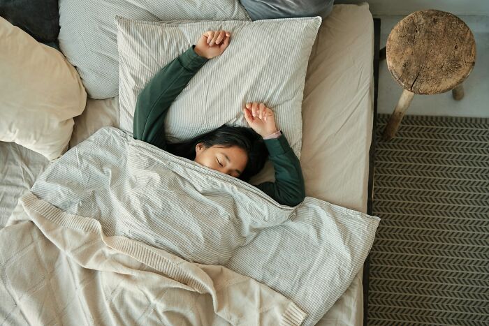 Person resting in bed under light blankets, showing a premium-tier zombie life hack related to sleep habits.