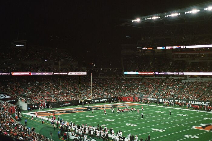 Nighttime football game with players on field and crowd in stadium, highlighting dumb ER visits and brain malfunction theme.