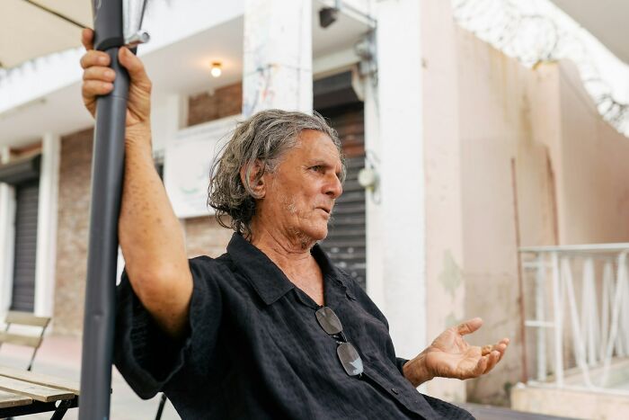 Older man in a black shirt gesturing while sitting outdoors, representing creepy advances faced and shut down by amazing women.