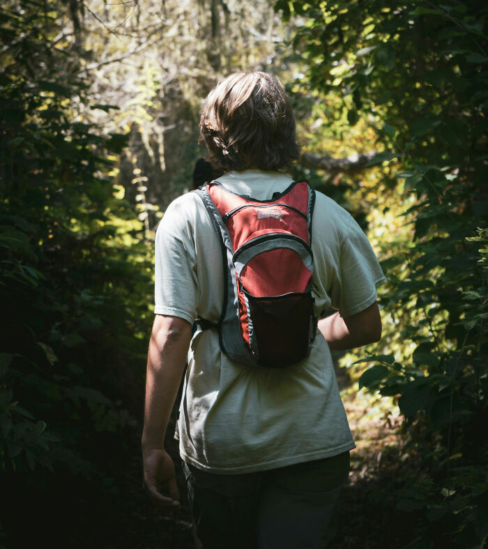 Person hiking through dense forest wearing a red backpack, capturing the essence of true scary camping and hiking stories.