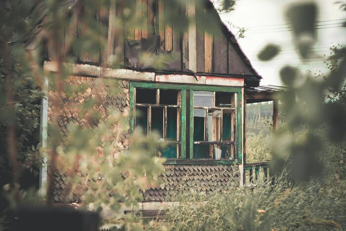 Abandoned run-down house with broken windows surrounded by overgrown vegetation, evoking urban explorer’s terrifying moments.