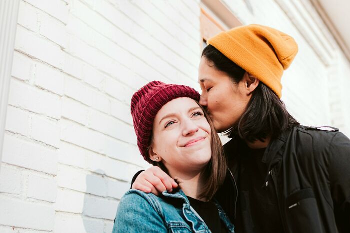 Two people wearing winter hats showing affection with a kiss, capturing a moment of cultural shock reactions from foreigners.