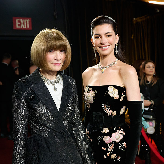 Anne Hathaway and Anna Wintour at a formal event, both dressed elegantly with jewelry and evening wear.