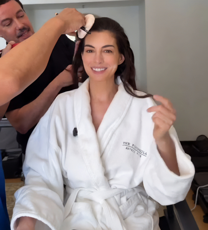 Anne Hathaway smiling in white robe getting her hair done, related to Oscars appearance and look concerns.
