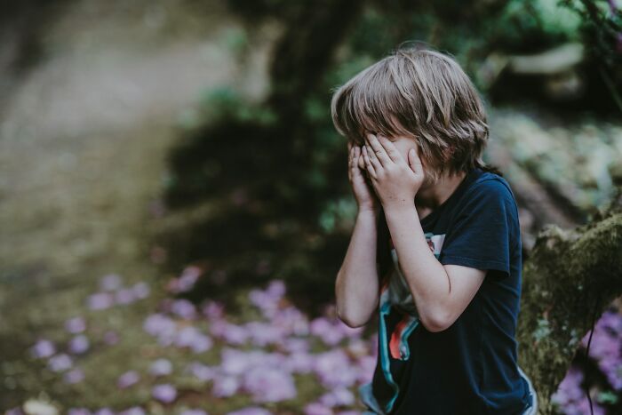 Young boy covering his face in a forest setting, capturing emotions related to 77 comebacks that were so on point.