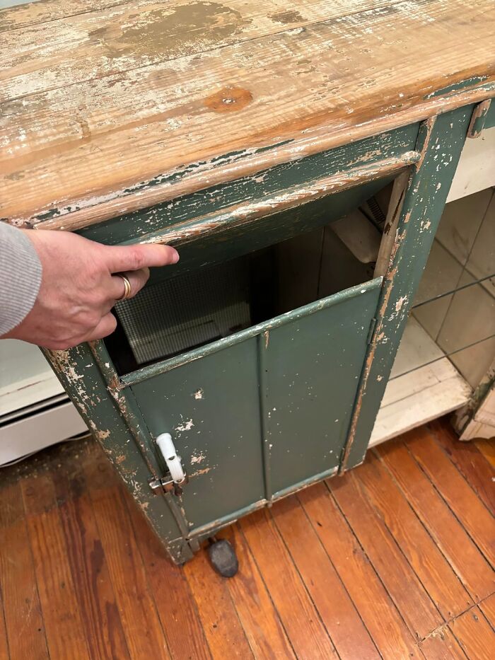 Hand pointing to a hidden compartment in an old, worn green cabinet in an old home with peeling paint.