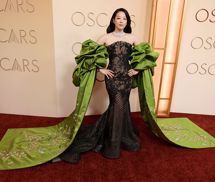 Actress wearing a black lace dress with oversized green sleeves and train, showcasing outrageous Oscars 2026 fashion looks.