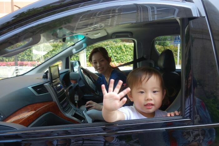 Child waving from car window with adult inside, capturing a moment that makes people question reality and mystery phenomena.