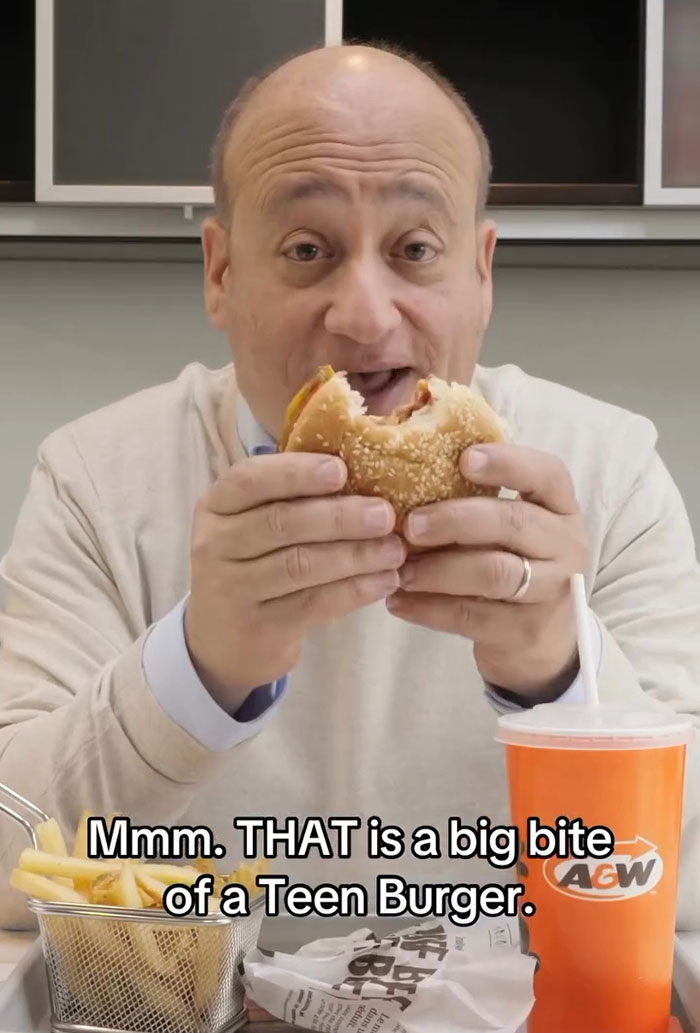 Man enjoying a big bite of a teen burger with fries and a drink, highlighting the burger battle in fast food industry.