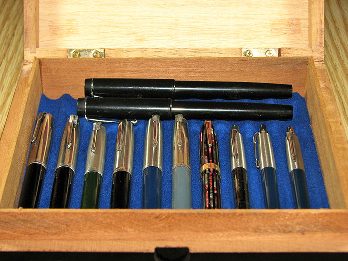 A wooden box displaying a collection of vintage pens on a blue felt interior, illustrating epic PR fails.