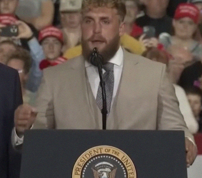 Man in beige suit speaking at podium with presidential seal, surrounded by crowd, illustrating epic PR fails.