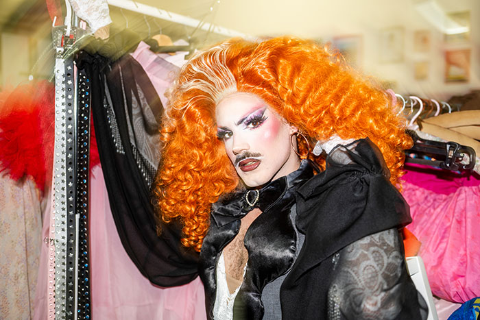 Person in elaborate orange wig and dramatic makeup posing in a colorful wardrobe setting illustrating epic PR fails.