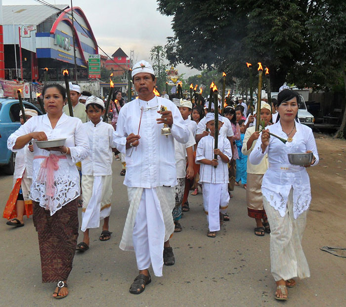 Bali locals in traditional attire holding torches during a cultural procession on public street amid Bali shutdown.