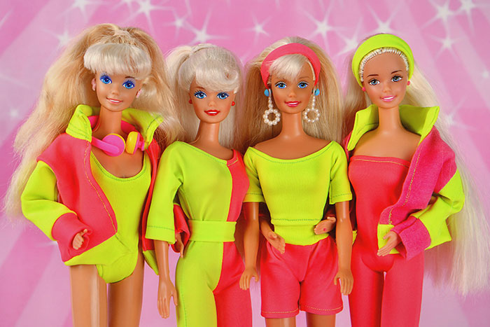 Quatro bonecas Barbie vintage vestidas com roupas neon brilhantes posando contra um fundo rosa estrelado. Quatro bonecas Barbie vintage vestidas com roupas neon brilhantes posando contra um fundo rosa estrelado.