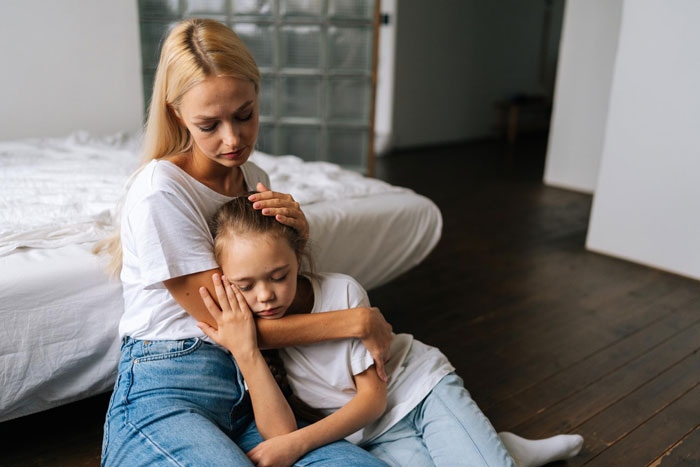 Mom comforting her upset daughter sitting on the floor after a best friend fight in a cozy bedroom setting.