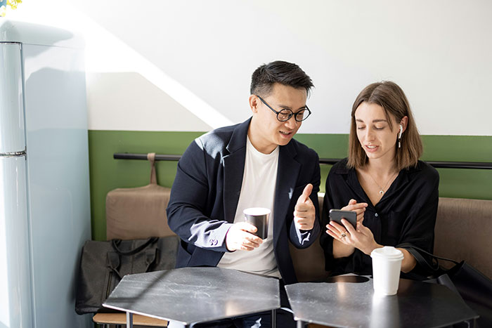 Couple sitting in cafe, man holding coffee cup and woman showing phone, highlighting romantic indifference and favorite foods.