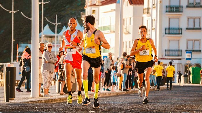 Three runners in bright sportswear competing in a race with spectators watching along the street during a sunny day PR fails event.