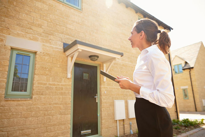 Woman inspecting house exterior with clipboard, acting as dorm inspector before boyfriend is allowed to move in.